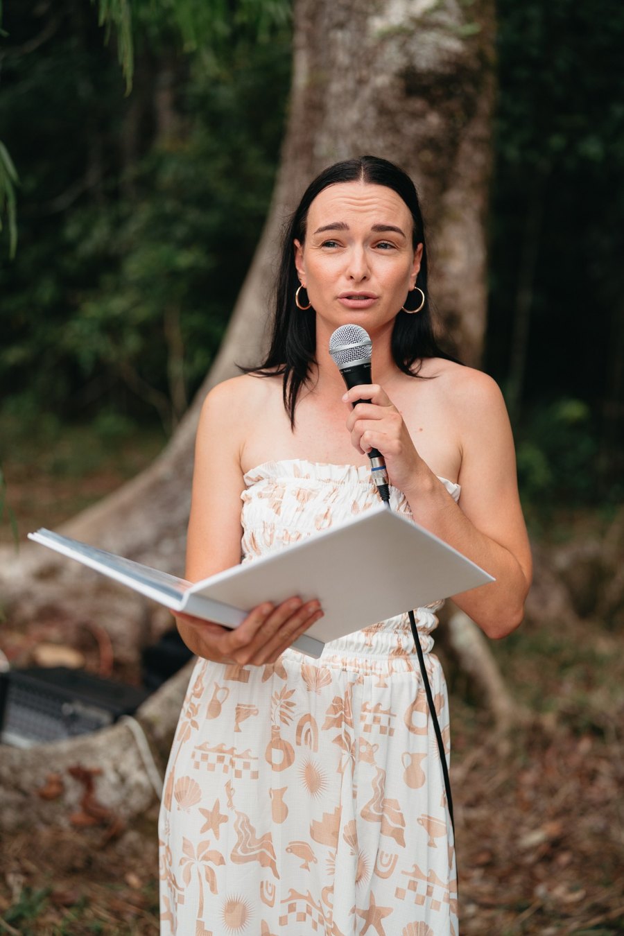 Ashley holding a microphone and ceremony folder outdoors