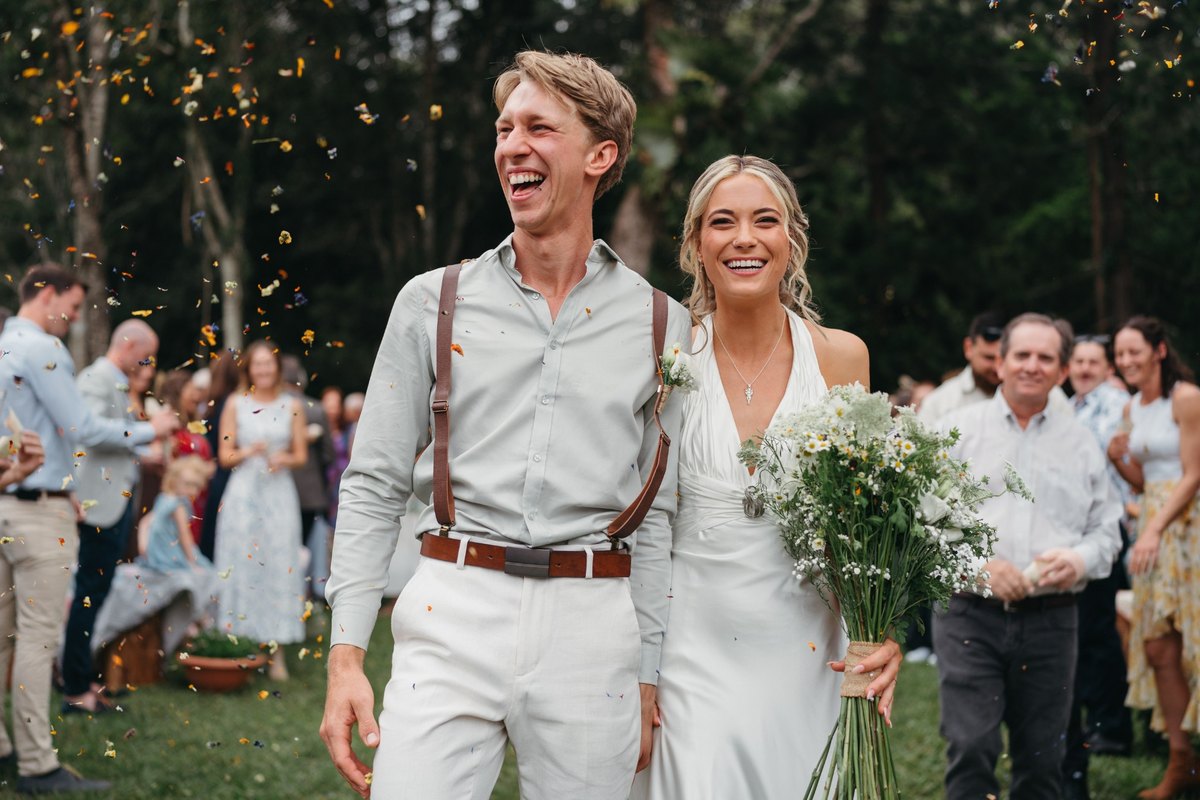 A newly married couple walking through confetti with wedding guests behind them